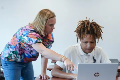 Professional helping a student on a laptop
